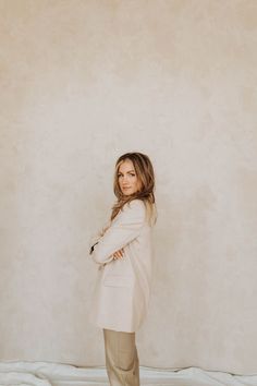 a woman standing in front of a wall with her arms crossed and looking at the camera