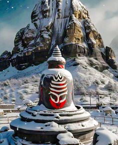 a statue in the middle of a snow covered field with mountains and rocks behind it