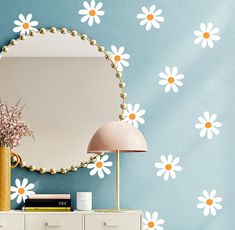 a mirror sitting on top of a dresser next to a wall with white daisies