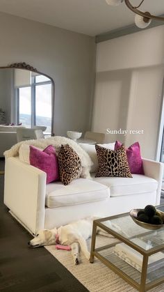 a living room with white couches and pink pillows on the back of each sofa