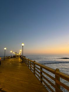 people are walking along the pier at sunset