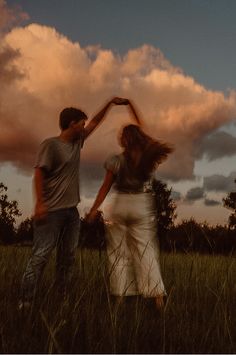 a man and woman dancing in a field with the sun setting behind them, as clouds loom overhead