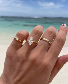 a woman's hand with three different rings on it and the ocean in the background