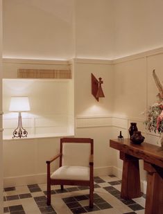 a chair and table in a room with flowers on the wall, vases and lamp