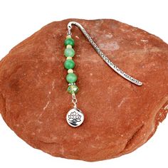 a green beaded bracelet with a silver charm on top of a red rock in front of a white background