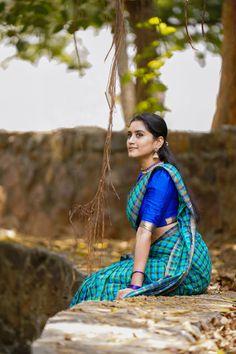 a woman in a blue and green sari sitting on a rock under a tree