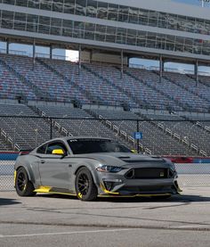 a grey mustang parked in front of a stadium bleachers with yellow stripes on it