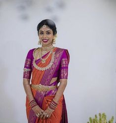 a woman in an orange and purple saree standing with her hands on her hips