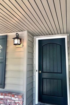 a black front door on a house next to a brick fire hydrant and lamp