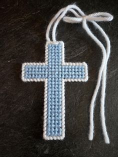 a crocheted cross is hanging from a string on a black surface with white and blue yarn