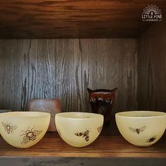 three yellow glass bowls sitting on top of a wooden shelf next to an owl statue