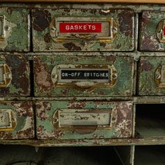 an old green cabinet with red labels on the drawers and one off sticker that says garage's