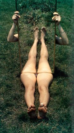 a woman laying on a swing in the grass with her feet up and legs down