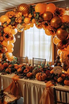 an orange and gold balloon arch decorated with pumpkins, greenery, and flowers