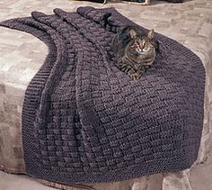 a cat laying on top of a bed covered in a knitted blanket and pillow