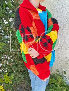 a woman standing in front of a wall wearing a colorful knitted sweater and jeans