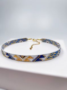 a blue and yellow beaded bracelet on a white surface with a gold clasp in the middle