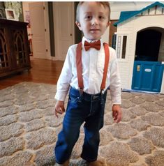 a young boy wearing a bow tie and suspenders standing in front of a dog house