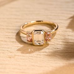 three stone ring sitting on top of a wooden table next to an orange and white diamond