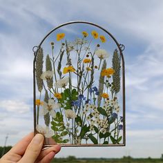 a hand holding up a piece of glass with flowers on it in front of a blue sky