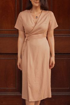 a woman standing in front of a wooden door wearing a tan dress and brown shoes