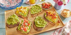 a wooden cutting board topped with slices of bread covered in guacamole