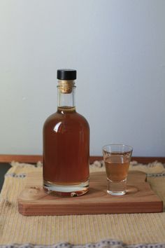 a bottle of alcohol sitting on top of a wooden table next to a glass filled with liquid