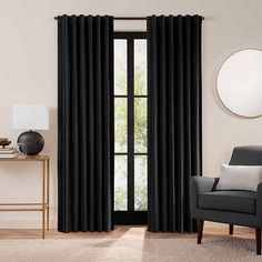 a living room with black curtains and a chair in front of a window that has a round mirror on the wall