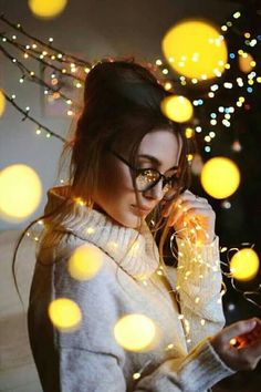 a woman wearing glasses is looking at her cell phone while surrounded by lights and garlands