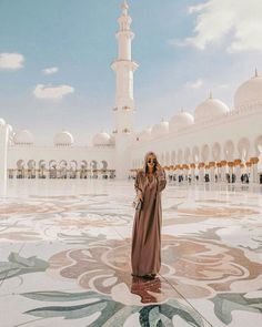 a woman standing in front of a white building with an intricate design on the floor