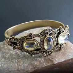 "This rich, unusually impressive bracelet is created from 90 year old stones set into our studio's original sculpture. The bracket is finely detailed and set with premium Swarovski smoke crystal. Three oval stones are vintage beauties from the 1930s which I acquired from a former exporter in Czechoslovakia. The bracket is mounted on a split shank cuff and will comfortably fit 7 to 8\" wrists. Hand burnished warm bronze finish. Entirely made in our Los Angeles studio. Choices:  AMETHYST EMERALD R Antique Jeweled Bangle Jewelry, Ornate Adjustable Jeweled Jewelry, Antique Gemstone Bracelet For Anniversary, Bohemian Jeweled Bracelets For Formal Occasions, Bohemian Gemstone Bracelets For Wedding, Bohemian Jeweled Bracelet For Formal Occasions, Bohemian Wedding Gemstone Bracelets, Unique Jeweled Bangle Jewelry, Antique Gemstone Bracelet For Gift