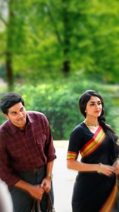 a man and woman are walking together in the park, one is wearing a colorful sari