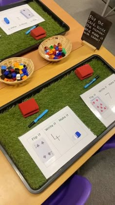 two trays filled with different types of toys on top of a wooden table covered in fake grass