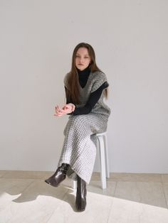 a woman sitting on top of a white chair wearing a gray and black blanket over her body