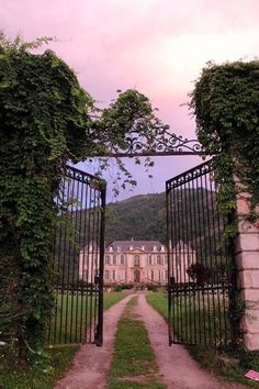 an iron gate leading to a large house with ivy growing on it's sides