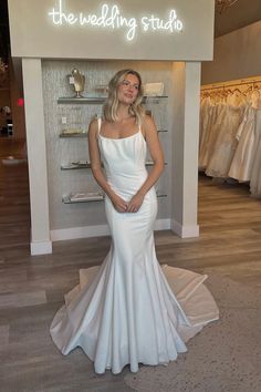 a woman standing in front of a wedding studio sign wearing a white dress and smiling at the camera