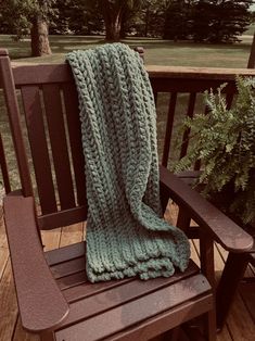 a green knitted blanket sitting on top of a wooden bench next to a potted plant