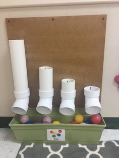 three white vases sitting on top of a green box filled with balls and plastic cups