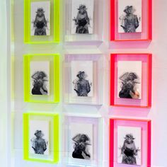 four framed pictures are hanging on the wall in front of some neon colored frames with black and white images