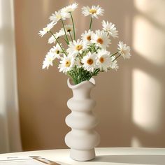 a white vase with daisies in it on a table next to a laptop computer