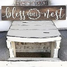 a wooden sign sitting on top of a white chair next to a wall with a wreath