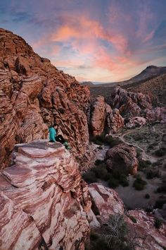 a man sitting on top of a large rock next to a desert area with mountains in the background