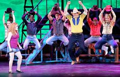 a group of people on stage with their arms in the air and one man wearing a cowboy hat