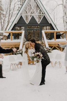 a bride and groom kissing in the snow at their winter wedding ceremony, surrounded by guests