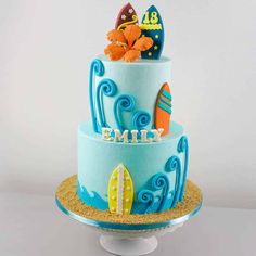 a three tiered cake with blue frosting and fondant surfboards on top