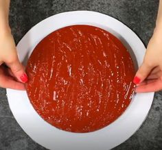 two hands holding a bowl of red sauce on a white plate with gray surface in the background