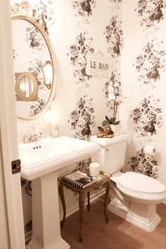 a white toilet sitting next to a sink in a bathroom under a mirror with flowers on it