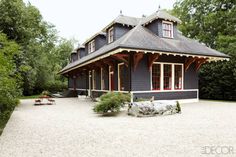 a black house in the middle of a gravel area with trees and bushes around it