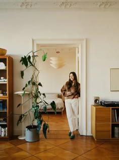 a woman standing next to a plant in a room with white walls and wooden floors