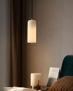 a lamp hanging over a bed next to a night stand with a book on it